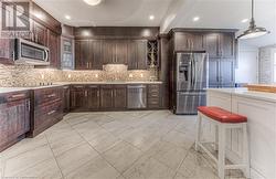 Kitchen featuring stainless steel appliances, dark brown cabinetry, hanging light fixtures, sink, and backsplash - 