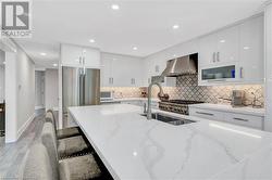 Kitchen with high end refrigerator, white cabinetry, a breakfast bar area, wall chimney exhaust hood, and light wood-type flooring - 