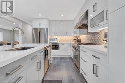 Kitchen featuring white cabinetry, dark hardwood / wood-style flooring, premium appliances, and wall chimney range hood - 