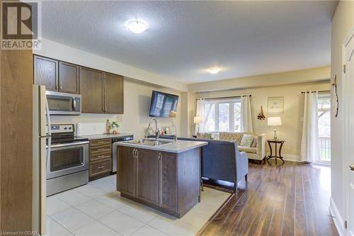 Kitchen featuring light wood-type flooring, dark brown cabinetry, stainless steel appliances, sink, and a center island with sink - 135 Samuel Drive, Arthur, ON 