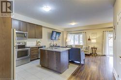 Kitchen featuring light wood-type flooring, dark brown cabinetry, stainless steel appliances, sink, and a center island with sink - 