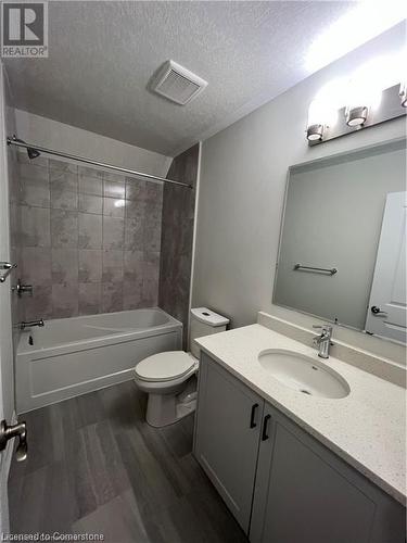 Full bathroom with tiled shower / bath, a textured ceiling, wood-type flooring, vanity, and toilet - 25 Isherwood Avenue Unit# 42, Cambridge, ON 