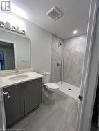 Bathroom with vanity, a textured ceiling, toilet, and tiled shower - 