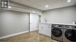 Clothes washing area with cabinets, light hardwood / wood-style flooring, sink, and washing machine and clothes dryer - 