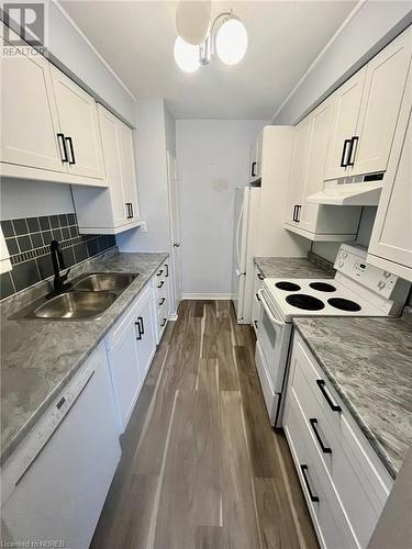 Kitchen featuring tasteful backsplash, white appliances, sink, dark hardwood / wood-style floors, and white cabinetry - 810 Main Street W Unit# 302, North Bay, ON - Indoor Photo Showing Kitchen With Double Sink