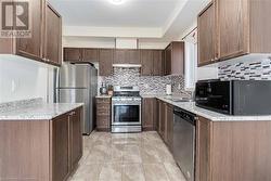 Kitchen featuring decorative backsplash, appliances with stainless steel finishes, light stone countertops, and sink - 