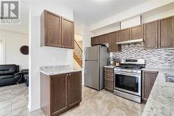 Kitchen featuring backsplash, sink, light tile patterned floors, appliances with stainless steel finishes, and light stone counters - 