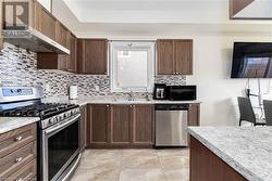 Kitchen with sink, tasteful backsplash, range hood, appliances with stainless steel finishes, and light stone counters - 