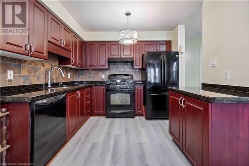 Kitchen with black appliances, dark stone counters, light wood-type flooring, decorative light fixtures, and sink - 42 Donnenwerth Drive, Kitchener, ON - Indoor Photo Showing Kitchen With Double Sink