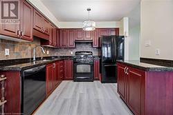 Kitchen with black appliances, dark stone counters, light wood-type flooring, decorative light fixtures, and sink - 