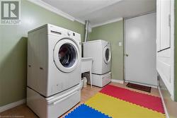 Laundry area with washer and dryer, light wood-type flooring, and ornamental molding - 