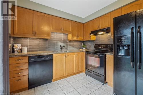 Kitchen featuring sink, tasteful backsplash, dark stone countertops, light tile patterned floors, and black appliances - 24 Kenyon Crescent Unit# 45, Grimsby, ON - Indoor Photo Showing Kitchen