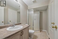 Bathroom with toilet, vanity, tile patterned floors, and a shower with door - 