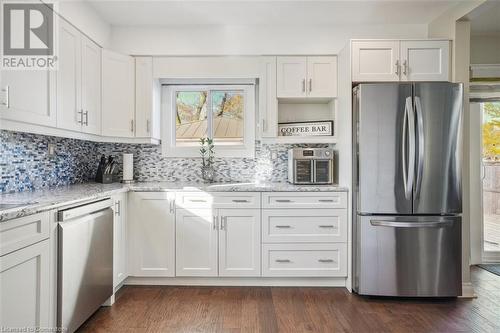 Kitchen with decorative backsplash, light stone counters, stainless steel appliances, dark hardwood / wood-style floors, and white cabinetry - 25 Rockwood Avenue, St. Catharines, ON - Indoor Photo Showing Kitchen With Upgraded Kitchen