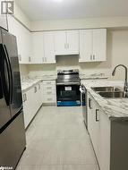 Kitchen with appliances with stainless steel finishes, light stone counters, sink, light tile patterned floors, and white cabinetry - 