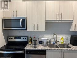 Kitchen featuring stainless steel appliances, light brown cabinetry, sink, and light stone countertops - 