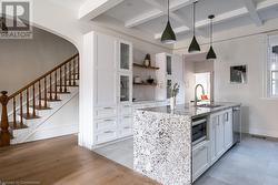 Kitchen with stainless steel microwave, sink, decorative light fixtures, a kitchen island with sink, and white cabinets - 