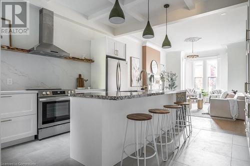 Kitchen featuring appliances with stainless steel finishes, wall chimney exhaust hood, pendant lighting, beamed ceiling, and white cabinets - 109 East Avenue S, Hamilton, ON - Indoor Photo Showing Kitchen With Upgraded Kitchen