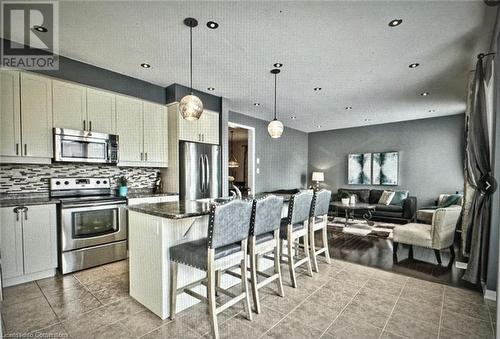 Kitchen featuring a kitchen bar, appliances with stainless steel finishes, decorative light fixtures, dark stone countertops, and a center island - 906 Farmstead Drive, Milton, ON - Indoor Photo Showing Kitchen With Upgraded Kitchen