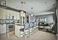 Kitchen featuring a kitchen bar, appliances with stainless steel finishes, decorative light fixtures, dark stone countertops, and a center island - 