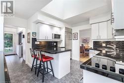 Kitchen featuring built in appliances, sink, white cabinetry, and backsplash - 