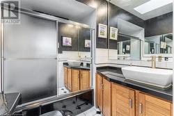 Bathroom with a skylight, tile patterned floors, vanity, tile walls, and enclosed tub / shower combo - 