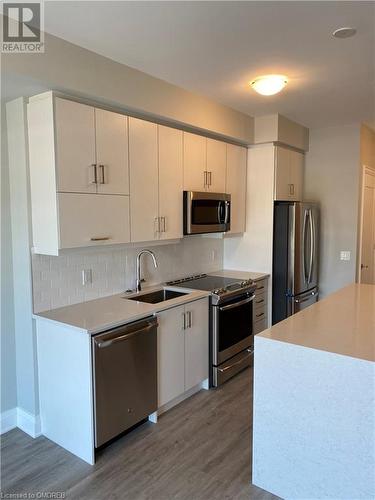 Kitchen featuring tasteful backsplash, stainless steel appliances, dark wood-type flooring, sink, and white cabinetry - 128 Grovewood Common Unit# 117, Oakville, ON - Indoor Photo Showing Kitchen With Stainless Steel Kitchen