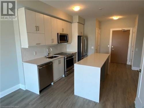 Kitchen featuring stainless steel appliances, sink, wood-type flooring, white cabinetry, and a kitchen island - 128 Grovewood Common Unit# 117, Oakville, ON - Indoor Photo Showing Kitchen With Stainless Steel Kitchen With Double Sink With Upgraded Kitchen