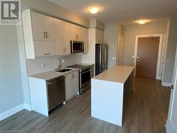 Kitchen featuring stainless steel appliances, sink, wood-type flooring, white cabinetry, and a kitchen island - 