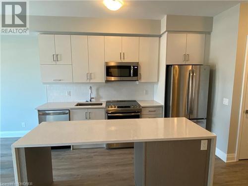 Kitchen with sink, a center island, stainless steel appliances, dark hardwood / wood-style flooring, and backsplash - 128 Grovewood Common Unit# 117, Oakville, ON - Indoor Photo Showing Kitchen With Stainless Steel Kitchen