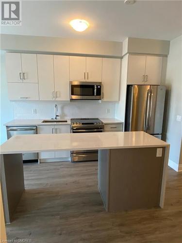 Kitchen featuring decorative backsplash, dark hardwood / wood-style flooring, stainless steel appliances, sink, and a center island - 128 Grovewood Common Unit# 117, Oakville, ON - Indoor Photo Showing Kitchen