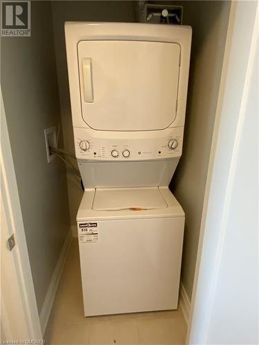 Laundry room with stacked washer and dryer and light tile patterned flooring - 128 Grovewood Common Unit# 117, Oakville, ON - Indoor Photo Showing Laundry Room