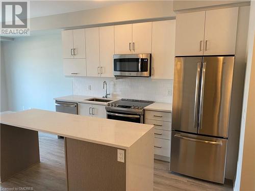 Kitchen featuring sink, light hardwood / wood-style flooring, a kitchen island, and appliances with stainless steel finishes - 128 Grovewood Common Unit# 117, Oakville, ON - Indoor Photo Showing Kitchen With Stainless Steel Kitchen With Upgraded Kitchen