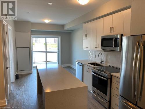 Kitchen with appliances with stainless steel finishes, tasteful backsplash, dark wood-type flooring, sink, and a kitchen island - 128 Grovewood Common Unit# 117, Oakville, ON - Indoor Photo Showing Kitchen With Stainless Steel Kitchen With Upgraded Kitchen