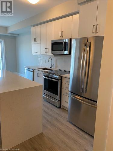 Kitchen featuring sink, tasteful backsplash, light hardwood / wood-style flooring, white cabinets, and appliances with stainless steel finishes - 128 Grovewood Common Unit# 117, Oakville, ON - Indoor Photo Showing Kitchen With Stainless Steel Kitchen