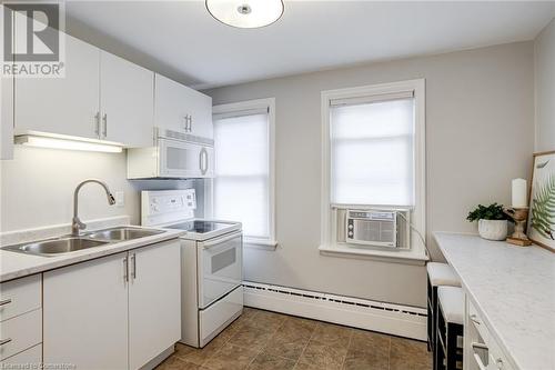 Kitchen featuring white appliances, cooling unit, sink, a baseboard radiator, and white cabinetry - 15 Empress Avenue, Hamilton, ON 