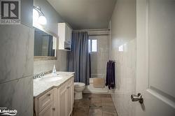 Full bathroom with shower / bath combo, tile patterned floors, toilet, vanity, and tile walls - 