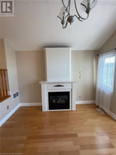 Unfurnished living room featuring a textured ceiling, light hardwood / wood-style floors, vaulted ceiling, and an inviting chandelier - 126 Peach Blossom Crescent, Kitchener, ON - Indoor With Fireplace