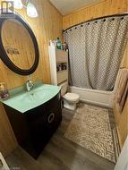 Full bathroom featuring wood-type flooring, toilet, wooden walls, vanity, and shower / tub combo - 