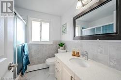 Bathroom with an enclosed shower, vanity, toilet, and tile walls - 