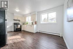 Kitchen with stainless steel fridge, black range with electric cooktop, a baseboard radiator, and dark hardwood / wood-style flooring - 