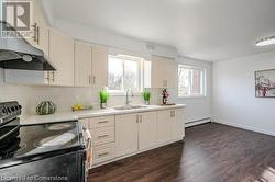 Kitchen featuring dark hardwood / wood-style floors, black range with electric stovetop, sink, and a baseboard radiator - 