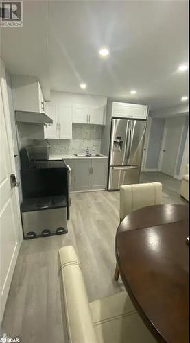 Kitchen featuring stainless steel refrigerator with ice dispenser, stove, decorative backsplash, white cabinets, and light wood-type flooring - 896 John Street Street Unit# B2, Innisfil, ON - Indoor Photo Showing Kitchen