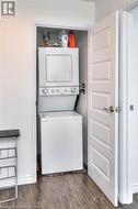 Washroom with dark hardwood / wood-style flooring and stacked washing maching and dryer - 