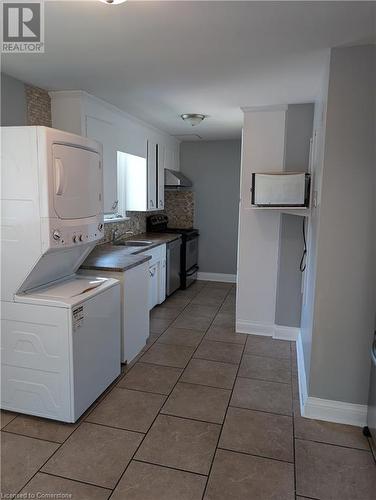 Kitchen featuring backsplash, white cabinets, dark tile patterned floors, stacked washing maching and dryer, and appliances with stainless steel finishes - 175 Oxford Street Unit# A, Kitchener, ON - Indoor Photo Showing Laundry Room