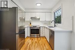 Kitchen with white cabinets, appliances with stainless steel finishes, light hardwood / wood-style floors, and sink - 