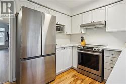 Kitchen with light hardwood / wood-style flooring, white cabinets, and stainless steel appliances - 