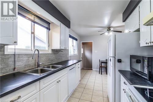 Kitchen featuring white cabinetry, sink, backsplash, white dishwasher, and light tile patterned flooring - 39 Keewatin Avenue, Kitchener, ON - Indoor Photo Showing Kitchen With Double Sink