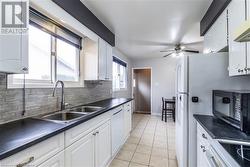 Kitchen featuring white cabinetry, sink, backsplash, white dishwasher, and light tile patterned flooring - 