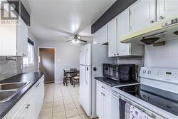 Kitchen with light tile patterned floors, white appliances, tasteful backsplash, and white cabinetry - 